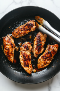 This image shows marinated chicken cooking in a hot pan, sizzling as it develops a crispy, golden brown crust.