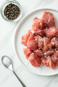 This image shows raw chicken pieces being generously seasoned with salt, pepper, and aromatic spices, ensuring a flavorful dish.