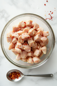 This image shows raw chicken pieces being coated with seasoning to enhance the flavor before cooking.