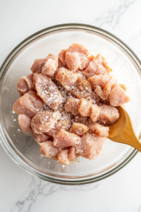 This image shows raw chicken pieces being seasoned with a blend of spices in a bowl, preparing them for marination.