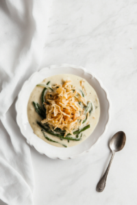 This image shows a serving of Crockpot green bean casserole being scooped into a dish, revealing the creamy green beans beneath a crispy layer of French fried onions.