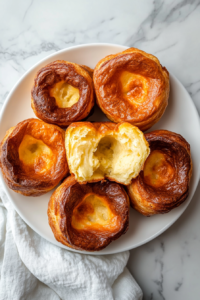 This image shows freshly baked Yorkshire puddings arranged on a white plate, ready to be served with a meal, showcasing their airy texture and crisp golden crust.