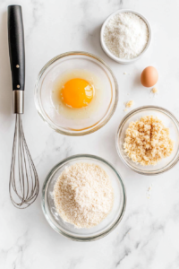 This image shows a dredging station with bowls of seasoned flour, eggs, and breadcrumbs, prepared for coating the chicken before frying.