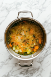 This image shows a pot of chicken soup gently simmering with herbs and vegetables, allowing the flavors to meld and the chicken to cook until tender.