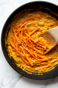 This image shows a skillet filled with coconut curry sauce gently simmering, thickening into a rich and creamy base for the Bang Bang Chicken and Shrimp.