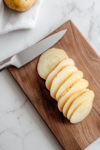 This image shows a sharp knife cutting the stacked potato layers into small, bite-sized portions, making them easy to fry and serve.