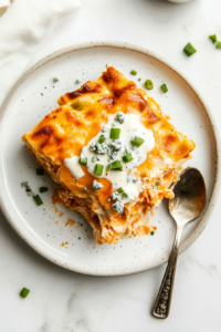 This image shows a freshly baked Buffalo Chicken Lasagna being sliced and drizzled with ranch dressing, garnished with green onions and blue cheese crumbles before serving.