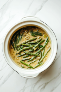 This image shows the green bean casserole simmering in the Crockpot, cooking slowly until the green beans are tender and the creamy mixture is heated through.