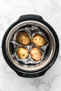 This image shows foil-wrapped potatoes inside a Crockpot during the cooking process, slowly baking to a perfectly tender and fluffy consistency.