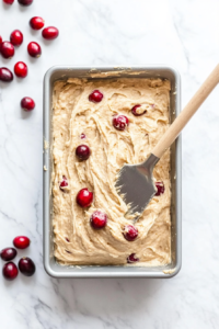 This image shows the prepared cranberry orange batter being poured into a greased loaf pan, ready for baking.