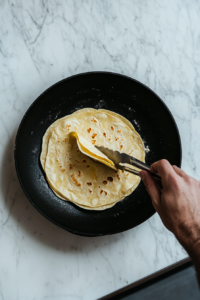 This image shows tortillas being warmed on a skillet, making them pliable and easier to roll without breaking.