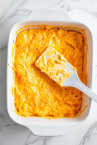 This image shows a creamy cheese mixture being evenly spread across the bottom of the prepared baking dish, forming the first layer of the lasagna.