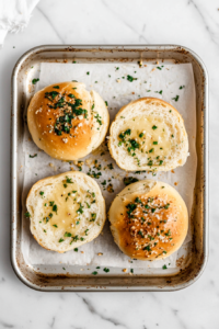 This image shows thick slices of fresh bread being brushed with a generous layer of homemade garlic butter, preparing them for baking into crispy, golden garlic bread.