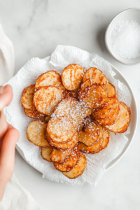 This image shows flaky salt being sprinkled over golden, crispy thousand-layer potatoes, enhancing their flavor and crunch.