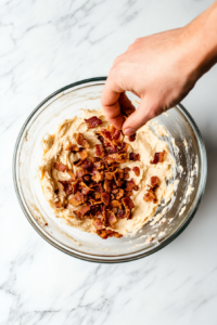 This image shows crispy bacon bits being crumbled and added to the mixture, providing a savory, smoky flavor.