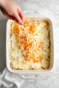 This image shows a generous amount of shredded cheese being sprinkled over the top of the lasagna, ensuring a gooey, cheesy finish after baking.