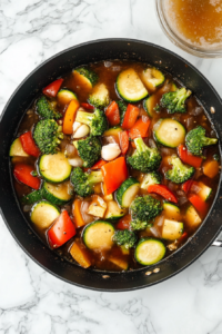 This image shows fresh vegetables, including broccoli and bell peppers, being stir-fried in a hot pan, enhancing their color and texture for the Chicken and Vegetables Stir Fry.