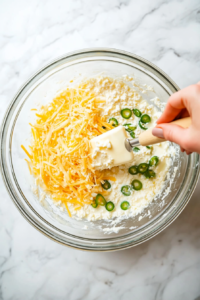 This image shows shredded Monterey Jack cheese, diced green chiles, and melted butter being added to the egg mixture for extra flavor and richness.