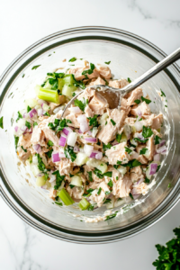 This image shows a top-down view of a spoon mixing all the ingredients together, ensuring the tuna salad is well combined and evenly coated with mayonnaise and seasonings.