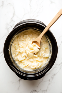 This image shows the cheesy potatoes being stirred mid-cooking to ensure an even, creamy texture throughout the dish.