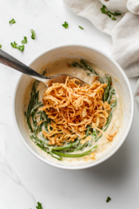 This image shows crispy French fried onions being stirred into the green bean and creamy soup mixture, adding a crunchy texture to the Crockpot green bean casserole.