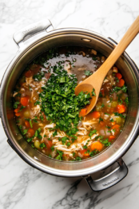 This image shows freshly chopped parsley being stirred into the shredded chicken soup, adding a vibrant color and a fresh, herbal aroma before serving.