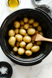 This image shows potatoes being stirred in the slow cooker, making sure they are evenly coated with oil, herbs, and seasonings for a well-balanced flavor.