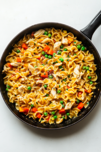 This image shows the chicken and noodles being stirred together in the creamy sauce, with final seasonings added for extra flavor.