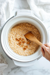 This image shows the oatmeal being stirred in the crockpot to combine all the flavors before serving, with soft apple pieces visible throughout the creamy mixture.