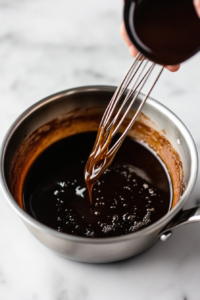 This image shows vanilla extract and buttermilk being added to the melted butter and sugar, enhancing the glaze with rich flavor.