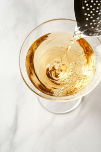 This image shows a bartender straining the perfectly mixed Vesper cocktail into a pre-chilled glass for a crisp and refined drink.