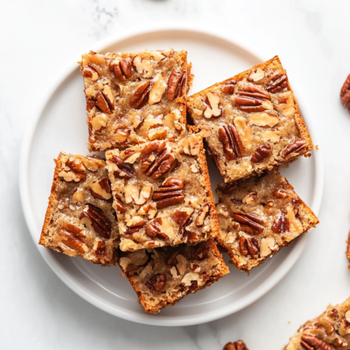 A plate of Sweet Alabama Pecan Bread, cut into square pieces with visible pecans, arranged neatly on a white round plate.