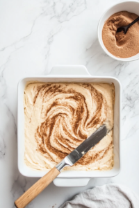 This image shows a knife or skewer swirling the cinnamon mixture into the batter, creating a beautiful marbled effect that enhances the cake’s flavor.