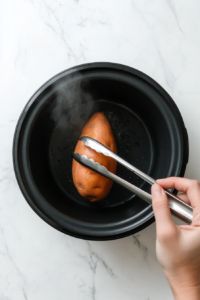 This image shows a person carefully removing soft, fully cooked sweet potatoes from the slow cooker, ready for serving.