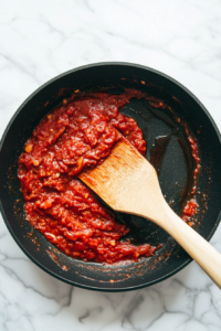 This image shows tomato paste and seasonings being mixed into the skillet, deepening the flavors of the sauce.