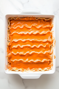 This image shows the final layer of pasta sheets being placed on top, followed by an even spread of the remaining cheese mixture.