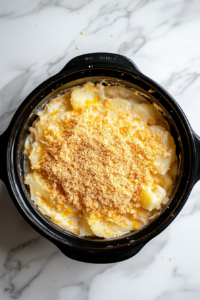 This image shows crumbled cheese-flavored crackers being sprinkled over the creamy cheesy potatoes, adding a crispy, flavorful topping just before serving.