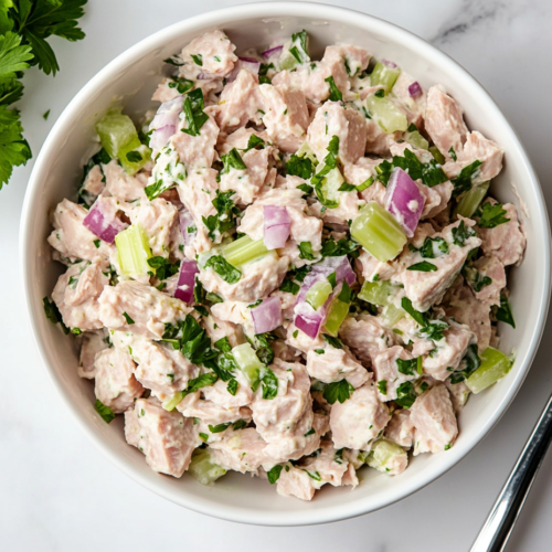 This image shows a fresh tuna salad served in a white bowl, seasoned with salt, pepper, and a squeeze of lemon juice for brightness.