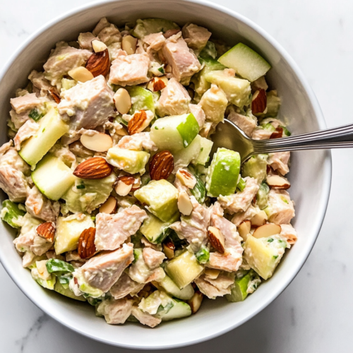 This image shows a refreshing tuna salad with apples, enriched with chopped avocados and almonds, served in a white bowl, ready to be enjoyed with any meal.