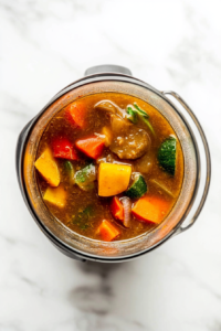 This image shows an immersion blender being used to partially blend the stew, creating a smooth yet hearty texture.