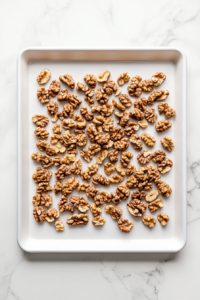 This image shows walnuts spread evenly on a baking sheet inside an oven, being toasted to enhance their crunch and bring out their deep, nutty flavor.