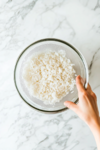 This image shows rice being rinsed under running water in a bowl, with the water turning cloudy as excess starch is removed for fluffier grains.