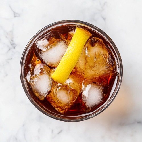 This image shows a glass filled with whiskey and Coca-Cola, served over chilled ice and garnished with a fresh lemon slice for a balanced and refreshing flavor.