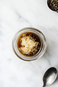 This image shows a hand whisking a homemade Asian-inspired dressing in a small bowl, blending ingredients like soy sauce, sesame oil, and rice vinegar to create a bold and tangy flavor.