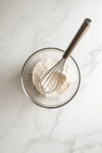 This image shows dry ingredients, including flour, baking powder, and salt, being whisked together in a mixing bowl to ensure even distribution.