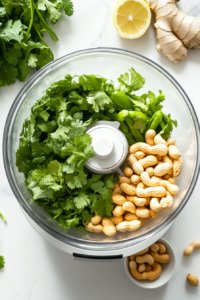 This image shows a white food processor on a pristine countertop with cilantro, garlic, ginger, and other ingredients being added to prepare the green chutney.