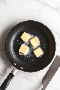 This image shows a non-stick skillet with butter melting to create a rich, golden base for frying the crab legs, ensuring a flavorful and crispy finish.