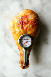 This image shows a meat thermometer inserted into a chicken lollipop, ensuring it reaches a safe internal temperature.