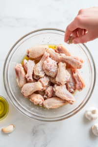 This image shows raw chicken wings being evenly seasoned with a blend of spices, ensuring every piece is packed with flavor before cooking.