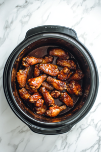 This image shows chicken wings simmering in a slow cooker, absorbing the rich honey BBQ sauce, becoming fall-off-the-bone tender and irresistibly flavorful.